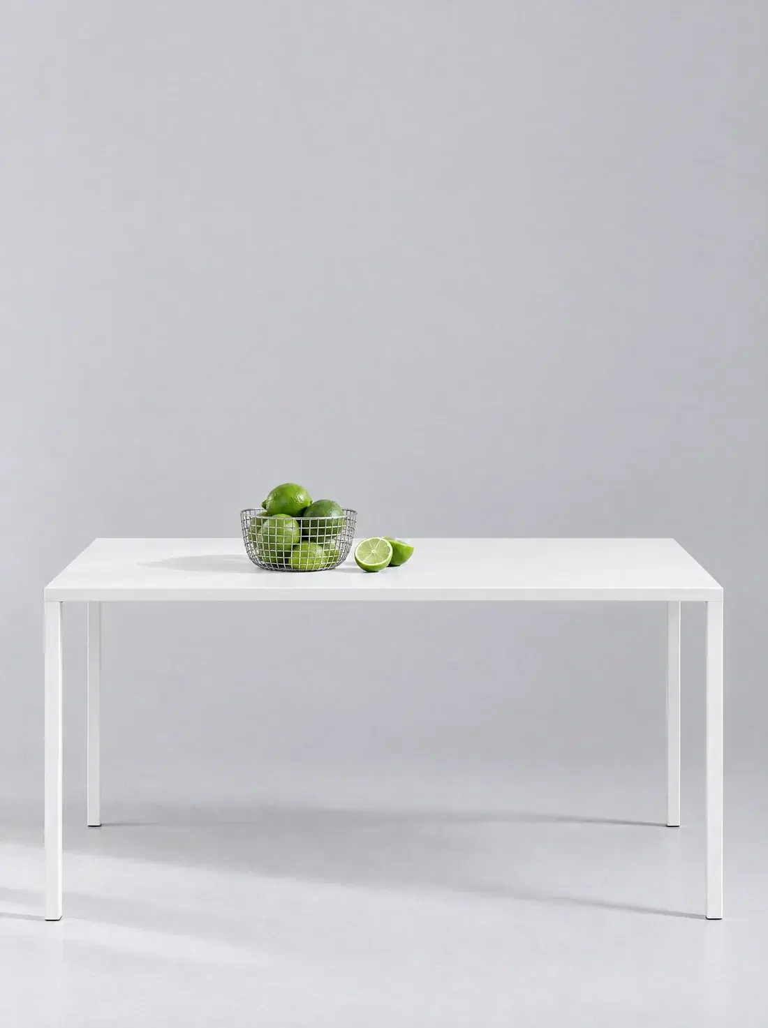 a small metal mesh basket of limes on a white table