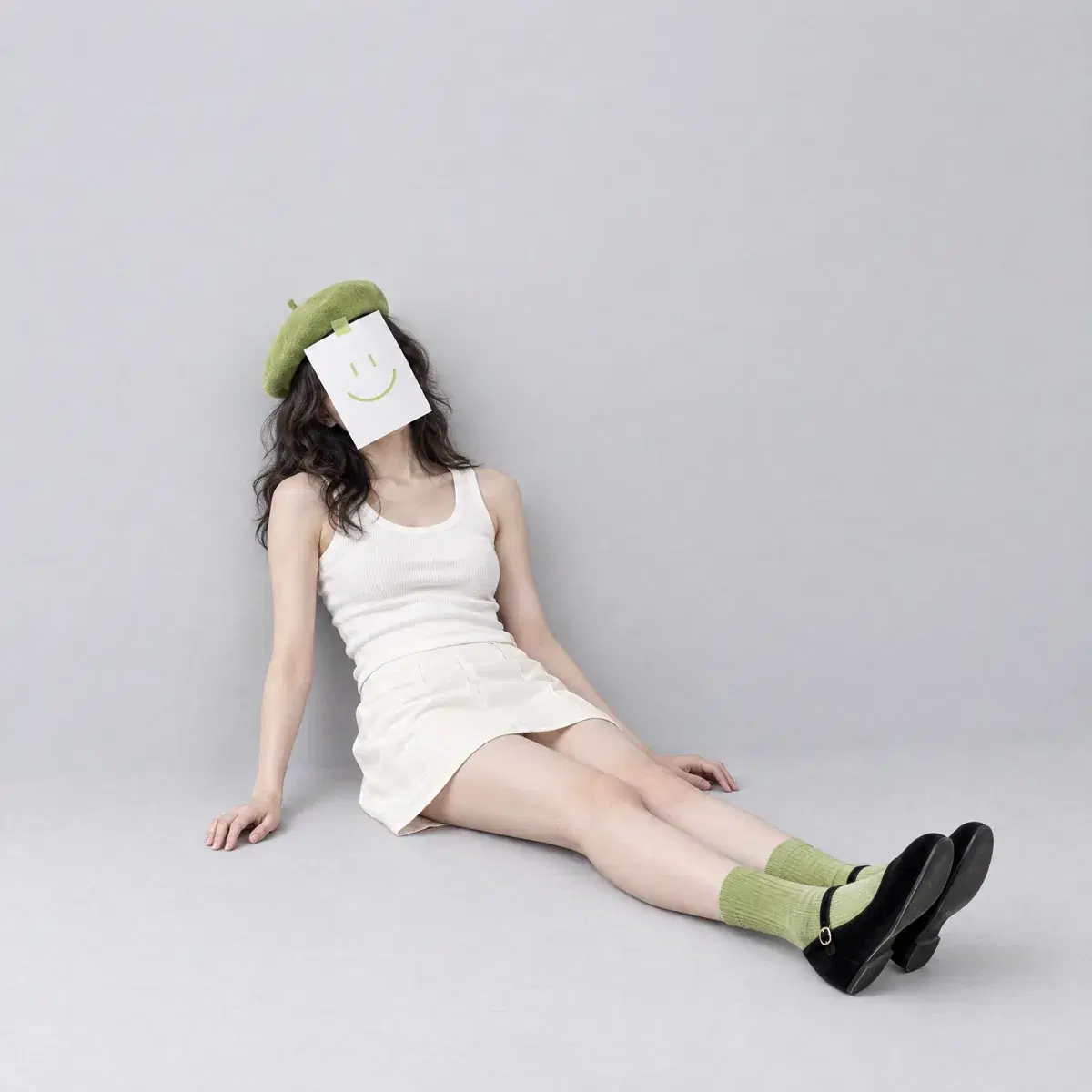 a woman sitting on the studio floor with a smiley-face paper over her face